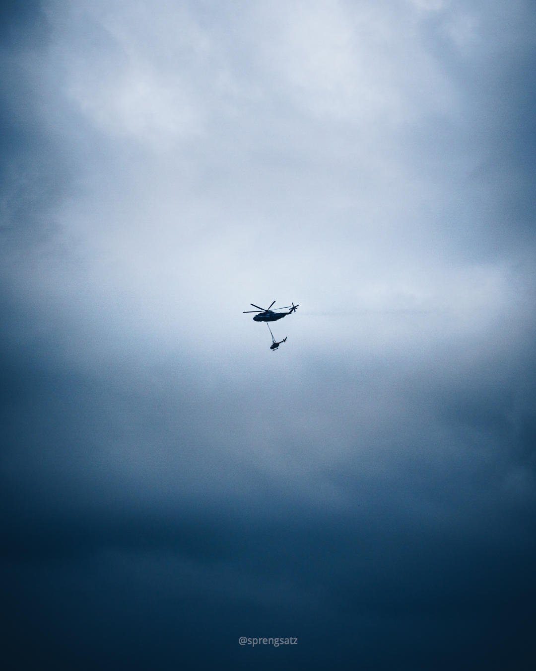 Hubschrauber transportiert einen (kleineren) Hubschrauber durch bewölkten Himmel