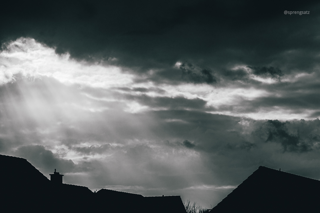 Sonnenstrahlen scheinen durch eine dichte Wolkendecke auf Hausdächer