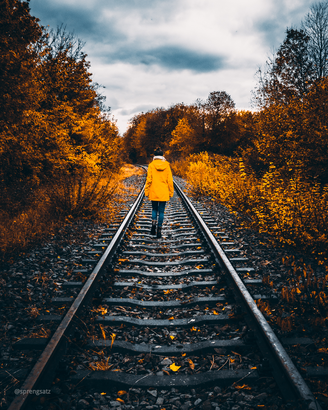 Frau in gelber Jacke läuft auf unbenutzten Bahngleisen der Zellertalbahn im Goldenen Herbst in Albisheim